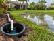Yard sump pump and discharge pipe beside standing water in a landscaped Florida lawn